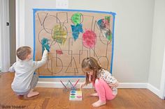 two young children playing with their art work on the floor in front of a wall