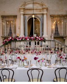 a table set up with flowers and candles for a wedding reception in front of an old building