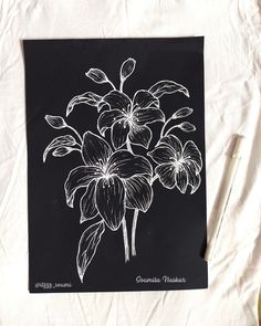 a black and white drawing of flowers on a piece of paper next to a pen