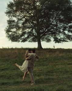 a man and woman are dancing in the grass under a tree