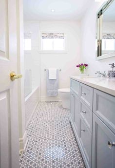 a white bathroom with gray cabinets and tile flooring on the walls is pictured in this image