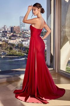 a woman in a long red dress standing by a window looking out at the city