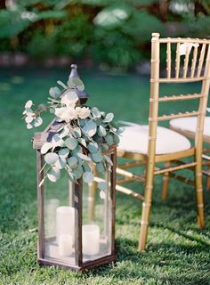 a lantern with flowers and candles on it next to an empty chair in the grass