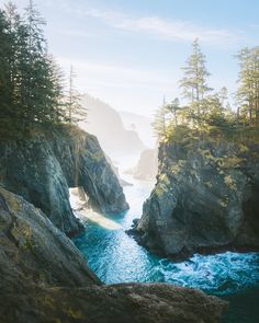 the ocean is surrounded by large rocks and pine trees on both sides of the water