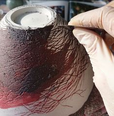 a person is painting a vase with red and black streaks on it's surface