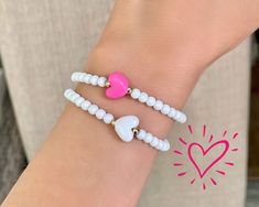 two bracelets with white beads and pink heart charms on the wrist, one for girls