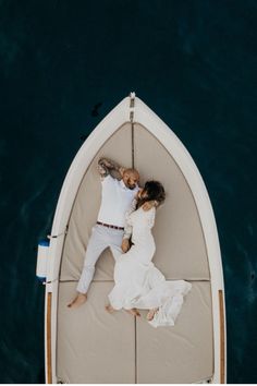 a man and woman laying in a boat on the water with their arms around each other