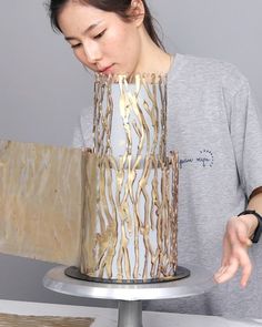 a woman standing in front of a white and gold cake on a silver platter