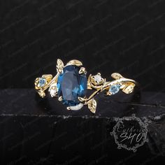 a ring with blue stones and leaves on the side, sitting on top of a black surface