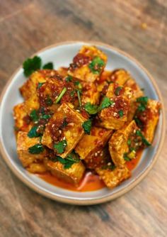 a white plate topped with tofu covered in sauce and garnished with parsley