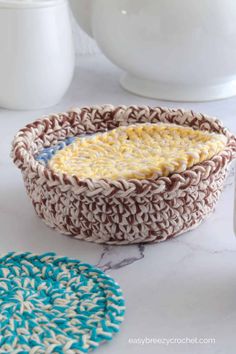 two crocheted baskets sitting on top of a counter next to cups and saucers