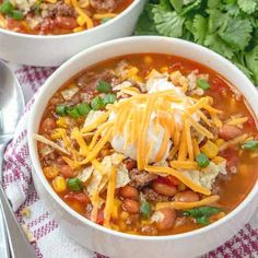 two bowls of chili and bean soup with sour cream on top, garnished with parmesan cheese