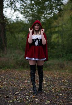 a woman wearing a red cape and boots standing in the woods with her hands on her hips