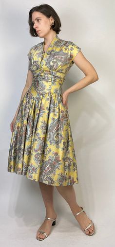 -->DESCRIPTION<-- Vintage 50s GORGEOUS golden yellow dress with matching bolero! So classic, slightly drop waist cut with full crinoline skirt and bow and rhinestone detail. Love the oversized paisley print and dreamy, almost southwest colour scheme. The bolero can be worn separately as a low cut crop top! No tags, dress is fully lined, does up with a steel zipper. -->CONDITION<-- Pristine condition! -->FABRIC<-- No tag to indicate, has a slight sheen, feels like a brushed cott Vintage Pleated Dresses With Fitted Bodice, Yellow Retro Vintage Dress For Garden Party, Retro Yellow Party Dress, Fitted Dress With Vintage Pattern For Vintage Events, Fitted Yellow Dress In 1950s Style, Yellow Fitted Dress In 1950s Style, Yellow Vintage Dress For Garden Party, 1950s Style Yellow Party Dress, 1950s Style Yellow Dress For Vintage Fashion