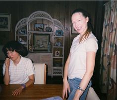 two people sitting at a table in front of a window and one person standing next to the table