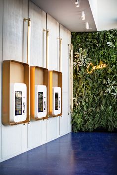 three cell phones mounted to the side of a wall with green plants on it's sides