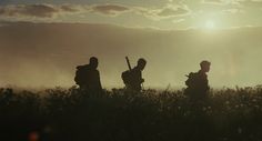 three people are standing in the grass with their guitars up to their backs as the sun sets behind them