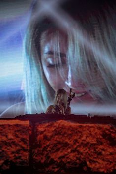 a woman standing on top of a stage with her hand up to her face and the screen behind her