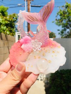 a pink and white mermaid figurine with flowers on it's shell is held up in the air