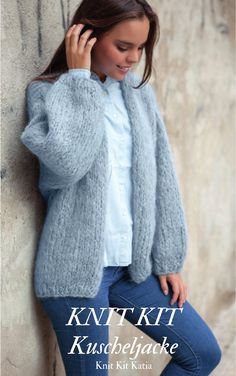 a woman leaning against a wall while talking on her cell phone and wearing a cardigan