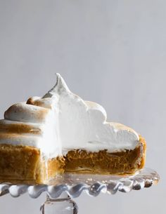 a slice of pumpkin pie on a glass cake plate with the rest of the pie in the foreground