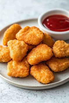 some fried food on a white plate with ketchup and dipping sauce in the background