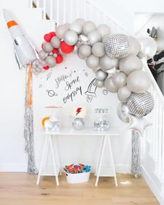 a room with balloons and decorations on the wall next to a white table in front of a staircase