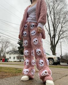 a woman standing on top of a sidewalk wearing pink crocheted pants with skulls