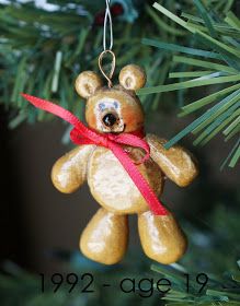 a brown teddy bear ornament hanging from a christmas tree with a red ribbon