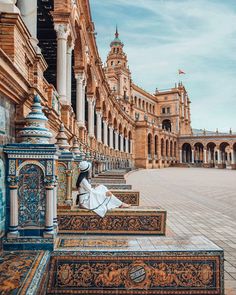 a woman sitting on the steps in front of a building with arches and columns,