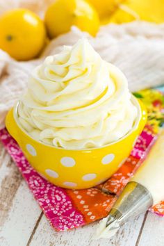 a yellow bowl filled with whipped cream on top of a table next to lemons