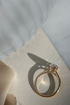 an engagement ring is sitting on top of a piece of white paper with a shadow