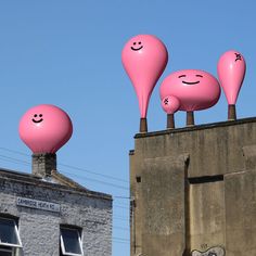 three large pink balloons with faces on top of a building in front of a blue sky