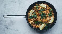 a skillet filled with rice, meat and lemons on top of a table