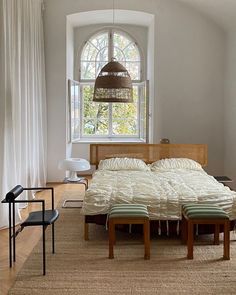 a bed sitting under a window in a bedroom next to a wooden table and chair