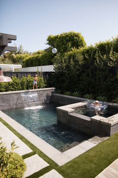 an outdoor swimming pool surrounded by greenery and trees with two people in the background