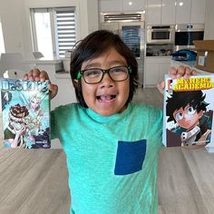 a young boy holding up two books in front of his face while standing on a kitchen counter