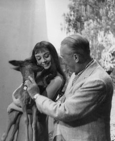 an old black and white photo of a woman petting a baby goat in front of a man