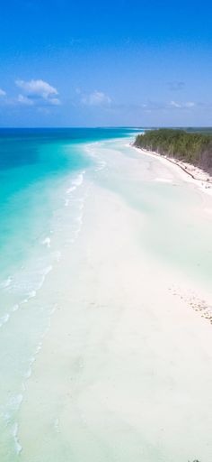 an aerial view of a beach with clear blue water and trees on the shore line