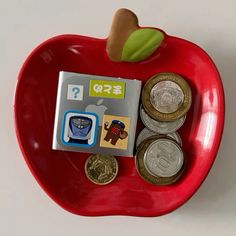 a red apple shaped tray with coins and stickers on it's side, sitting next to a coin holder