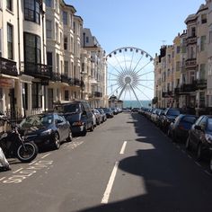 cars parked on the side of a street next to tall buildings and a ferris wheel