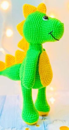 a crocheted green and yellow toy dinosaur on a wooden surface with lights in the background