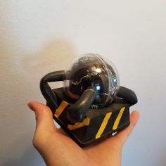 a hand is holding a toy with a black and yellow design on it's face