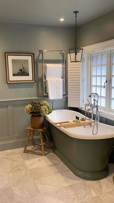 a bathroom with a claw foot tub and white tile flooring, framed pictures on the wall