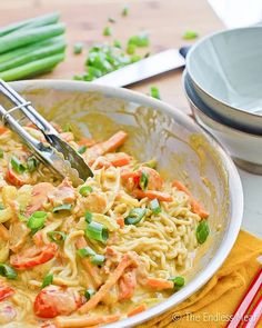 a bowl filled with noodles and vegetables on top of a table next to green beans