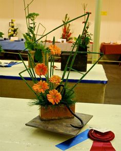 an arrangement of orange flowers in a pot on a table with ribbons and decorations around it