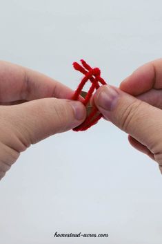 two hands holding red string together to make an ornament