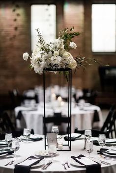 an elegant centerpiece with white flowers and greenery sits on top of a round table