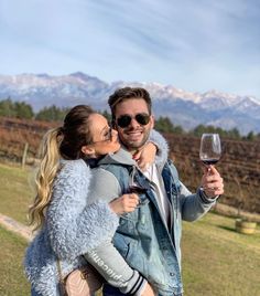 a man and woman are holding wine glasses in front of the mountains with snow - capped peaks behind them