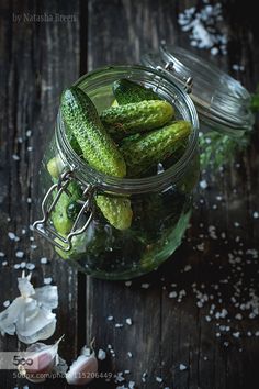 some pickles are in a glass jar on a wooden table with salt scattered around them